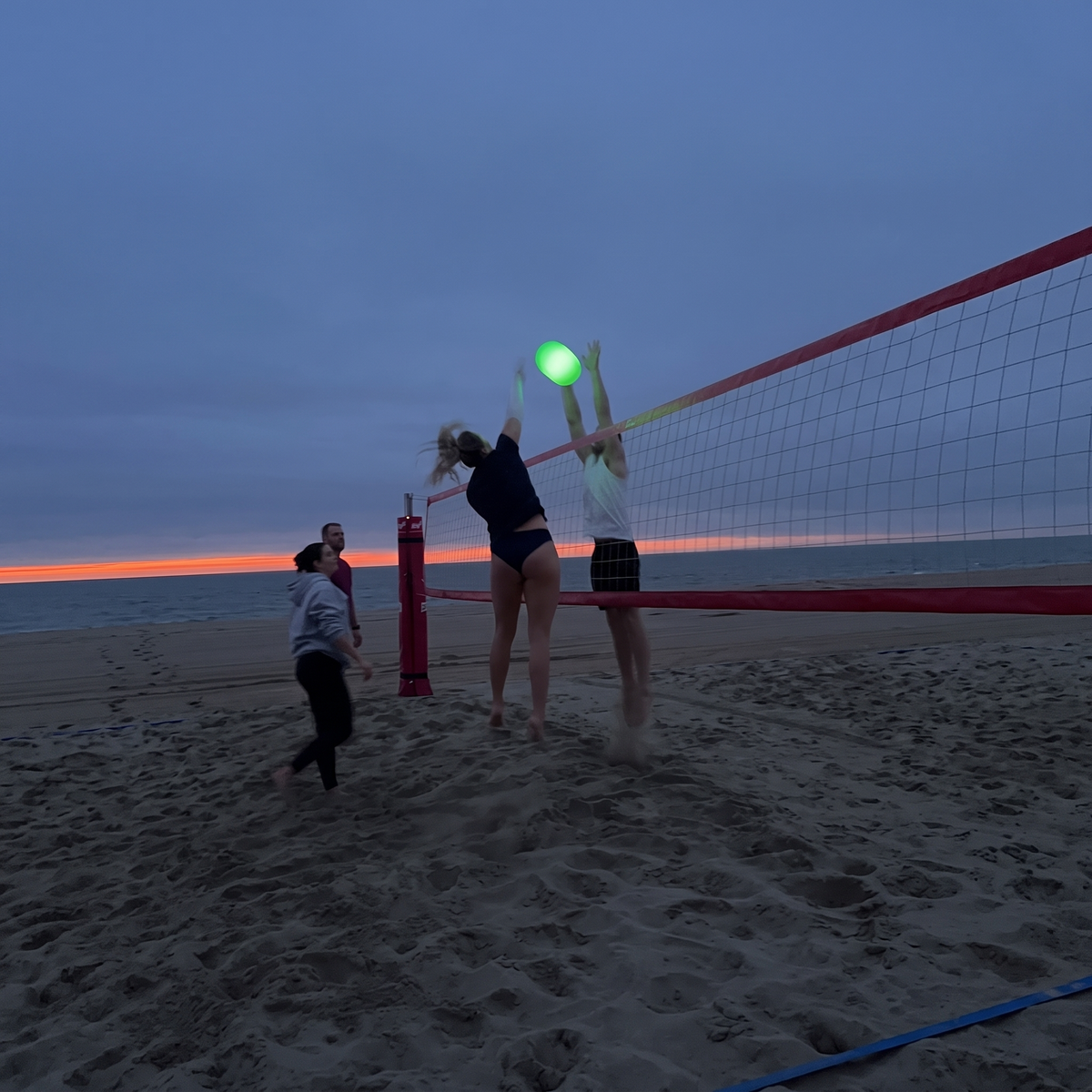 Freunde spielen abends am Strand mit dem leuchtenden Leuchtvolley